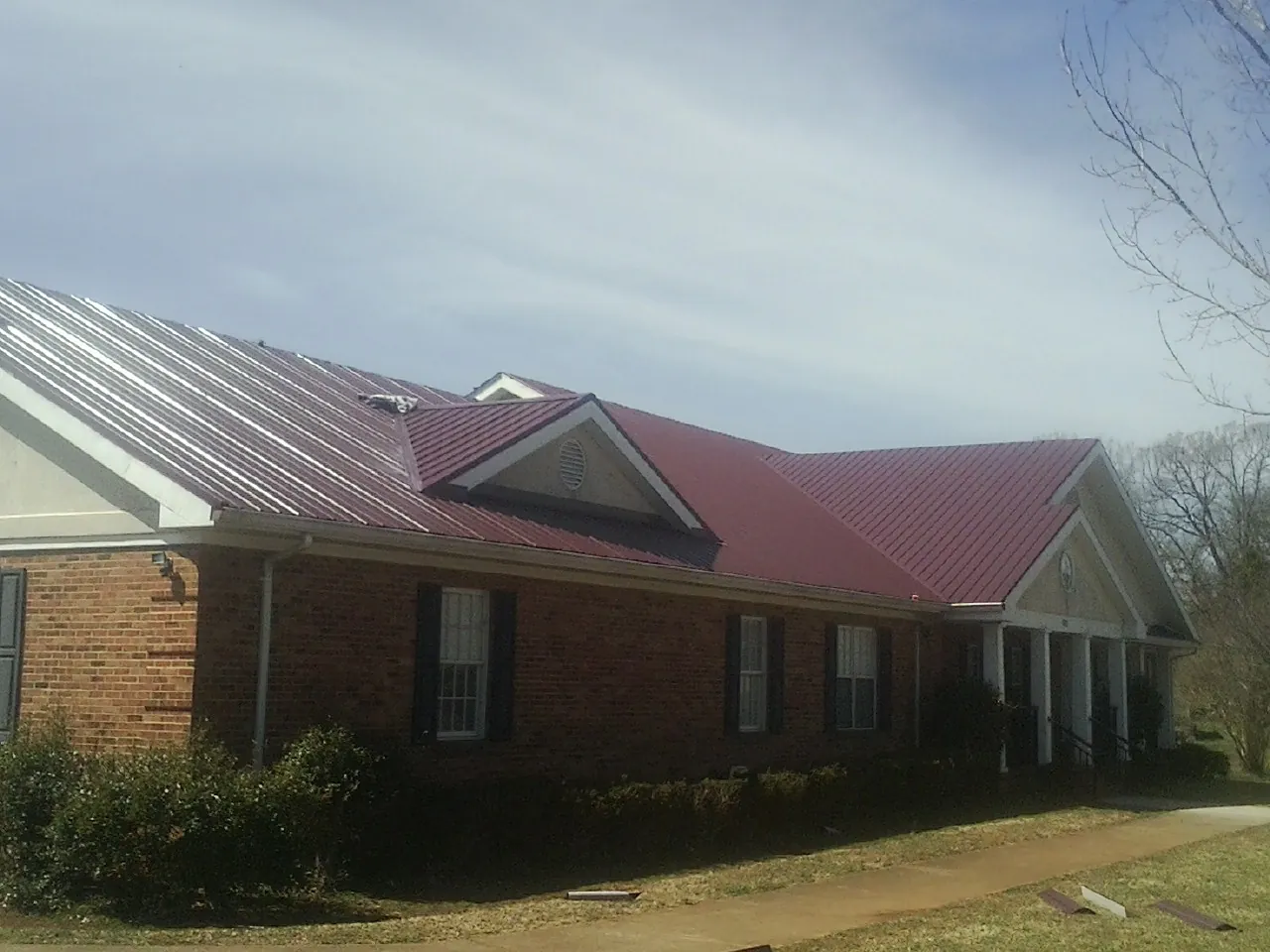 Red metal roof with gabled entries on a long brick building, from a Hail Damage Roof Repair job in Hostetter