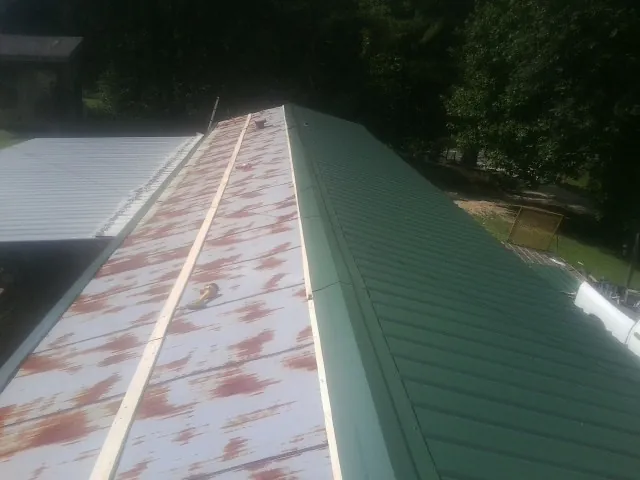 Old rusted panels beside newly installed green metal roofing — Wind Damage Roof Repair by Roofing Brothers in Hostetter