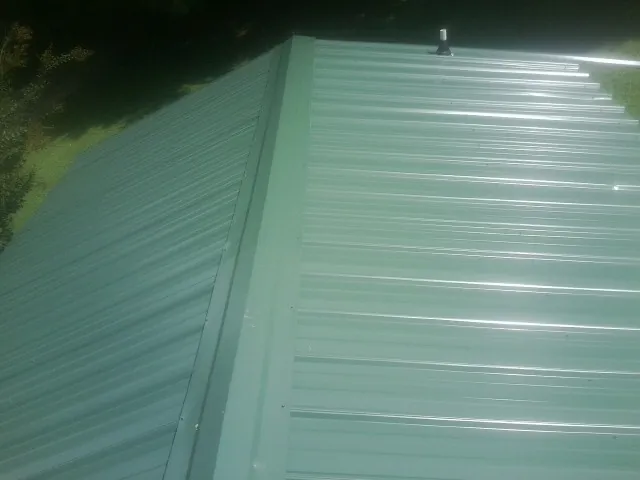 New green metal panels meeting at the ridge of a roof — Flat Roof Repair work by our crew in Hostetter