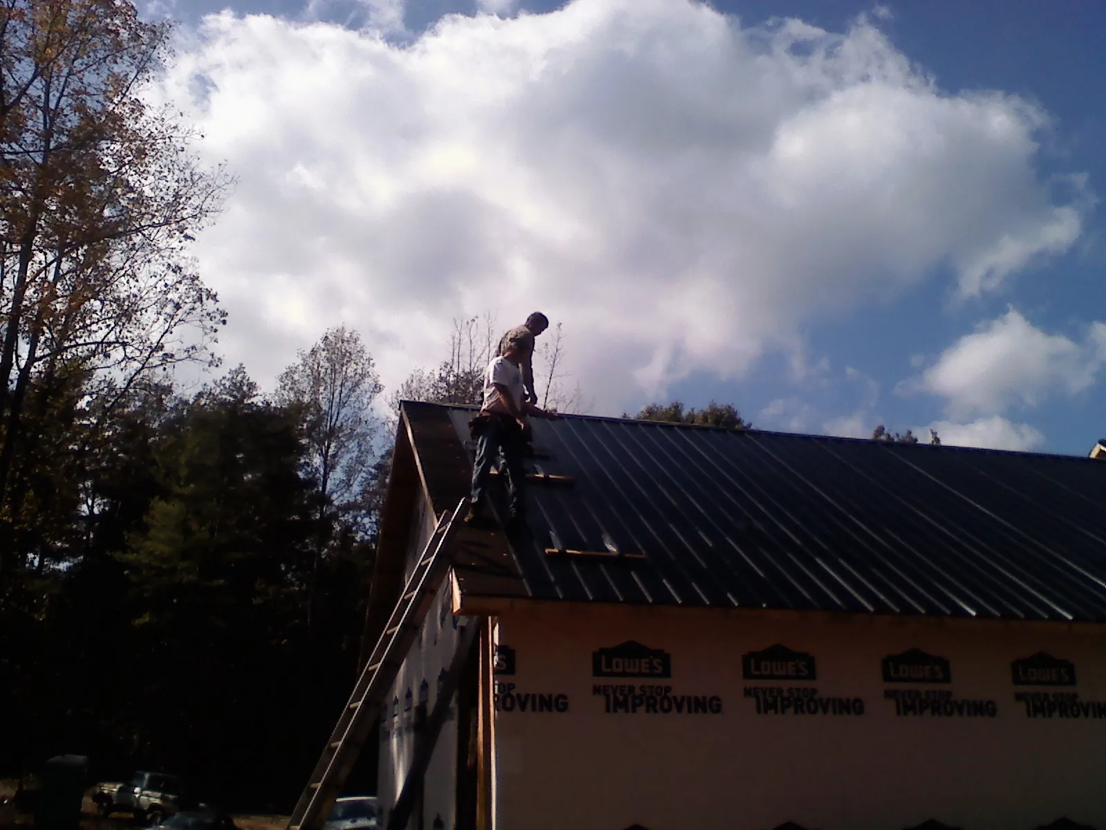 Roofer fastening dark metal panels high against a cloudy sky, from a Roof Inspection job in Hostetter