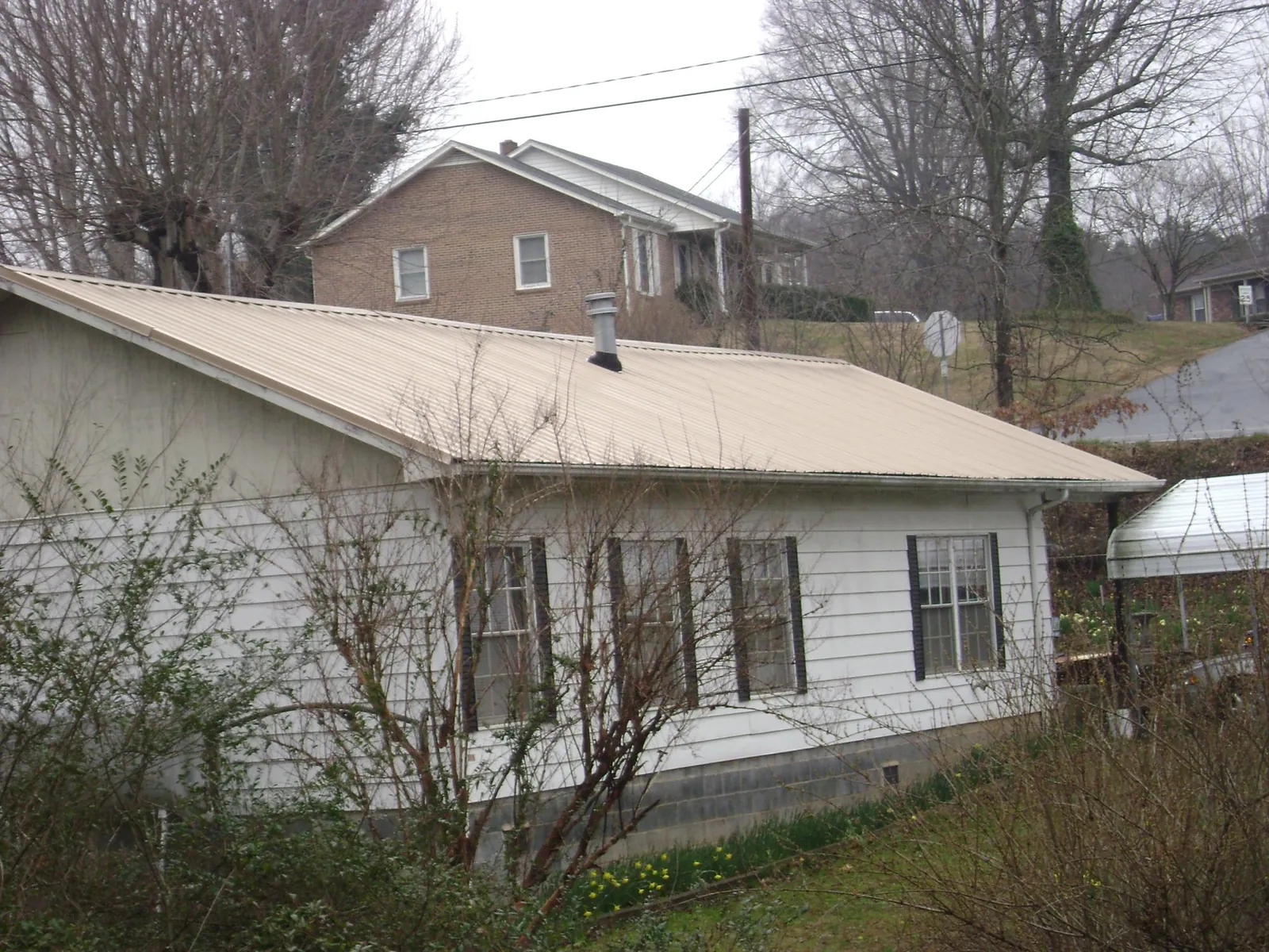 Tan metal roof on a white sided house set into a hillside — Commercial Roofing by Roofing Brothers in Hostetter