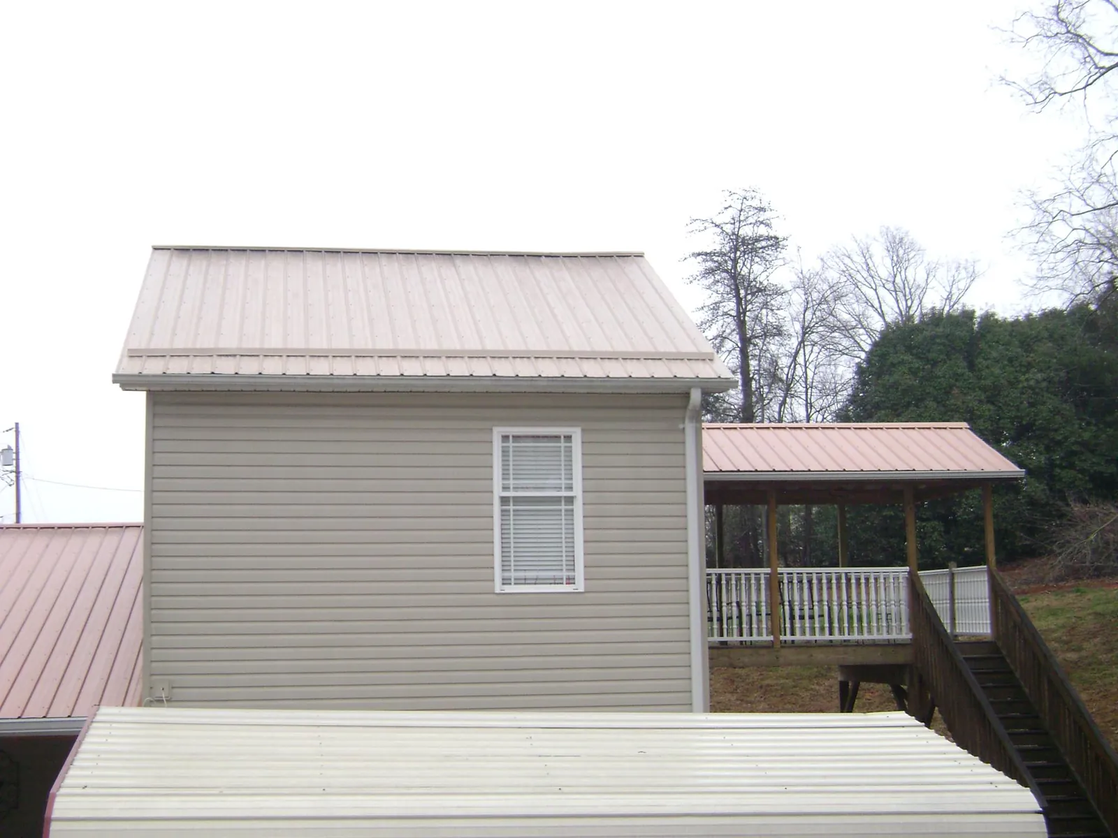 Tan metal roofs on a two story addition and attached porch, from a Roof Replacement job in Hostetter